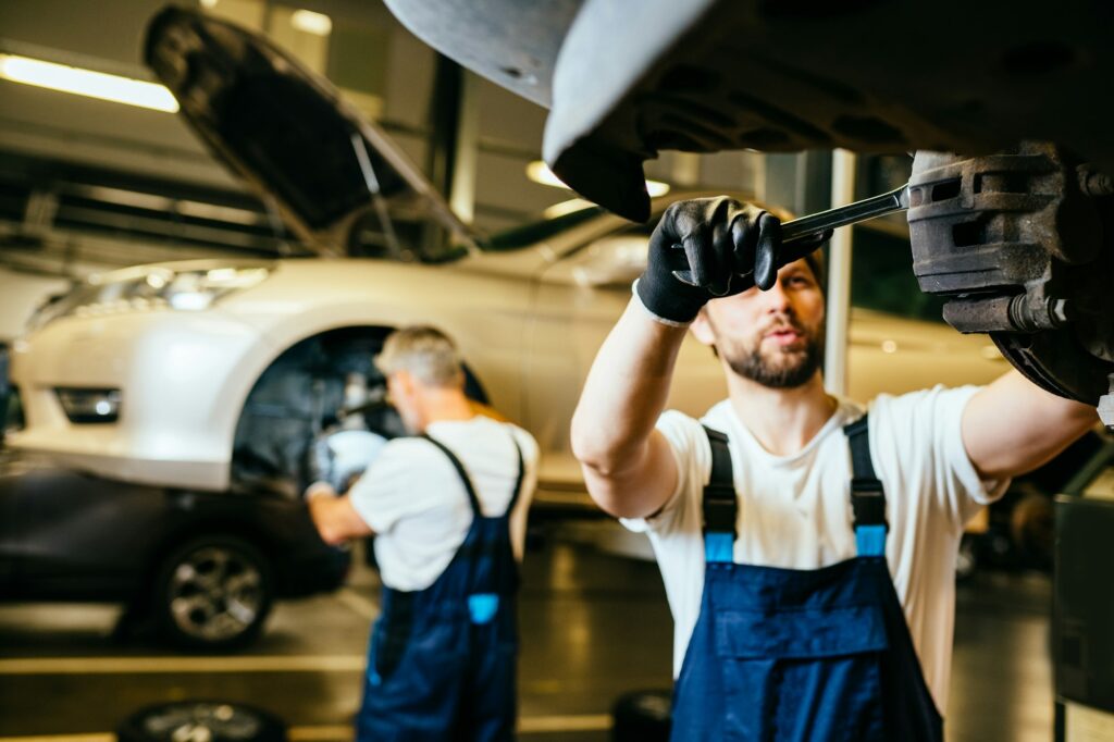 Mechanic in work at the auto service. Two car mechanic diagnosing vehicle at the auto service.
